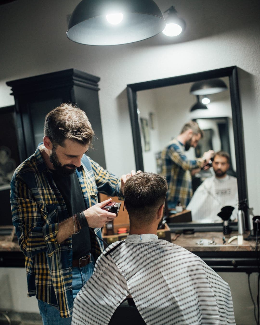 Barbeiro cortando o cabelo de um cliente com máquina, dentro da barbearia