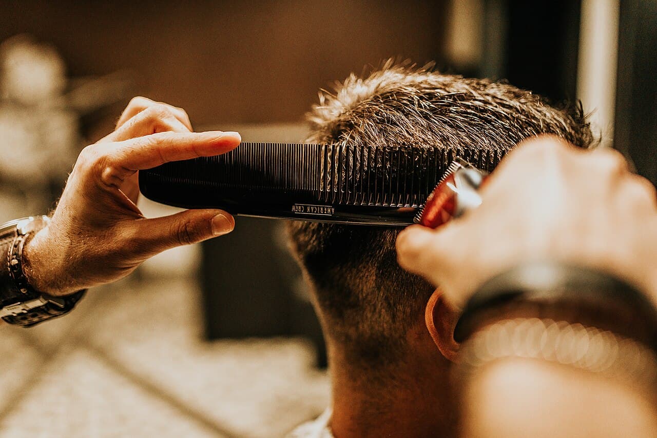 Barbeiro finalizando um corte masculino com pente e máquina