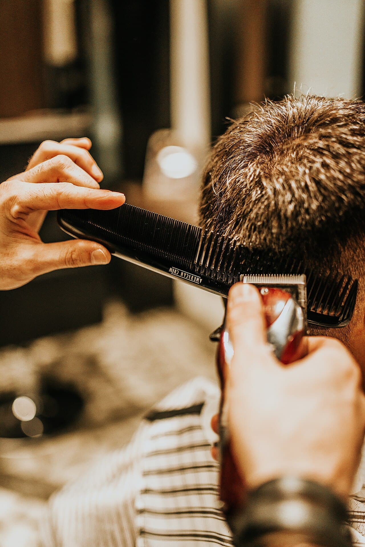 Barbeiro alinhando o corte de um cliente com pente e máquina